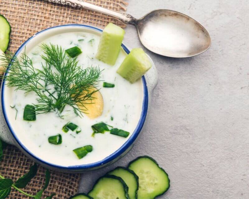 W małym garnuszku podano biały chłodnik przyozdobiony ogórkami, jajkiem i koperkiem.