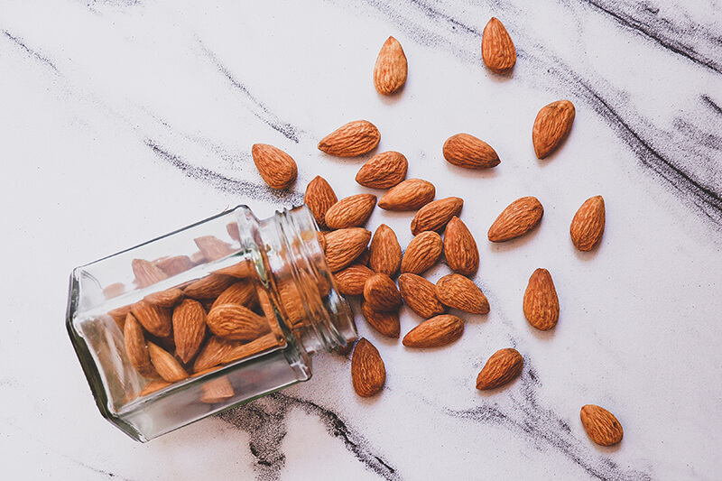 Na stole rozsypano migdały ze szklanego słoiczka idealnego do przechowywania orzechów.